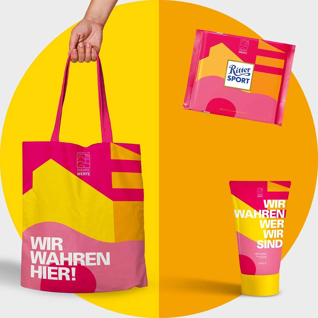 jutebeutel, schokoladentafel und tube als werbemittel im pink-gelben welterbe-design, aufdruck »wir wahren hier!«