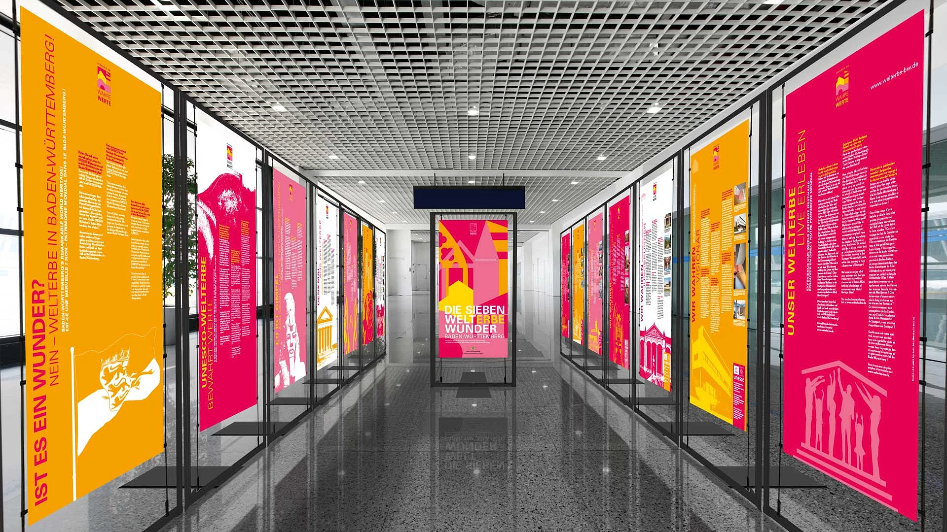 ausstellungsgang mit hängenden bannern in pink und gelb, die durch die welterbestätten führen