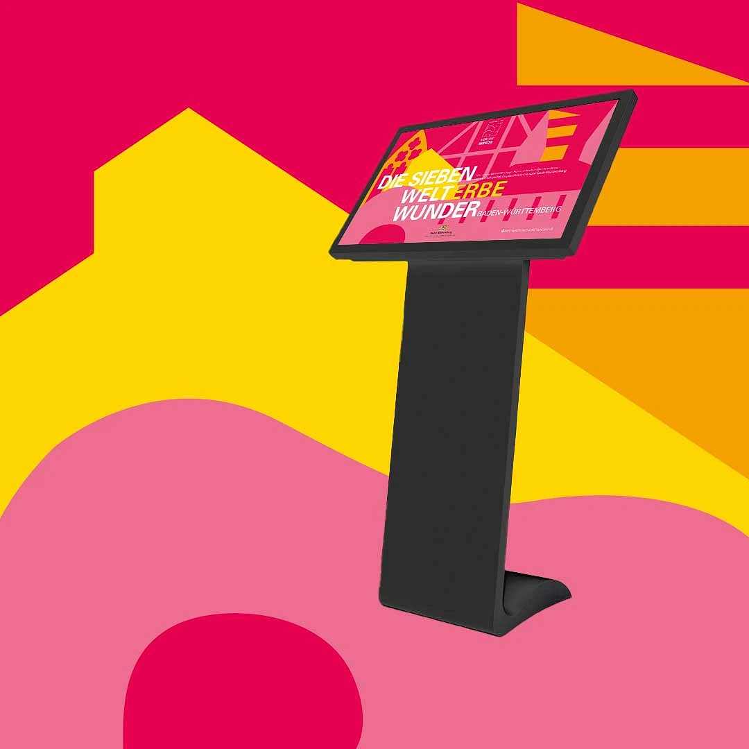 medienstele mit touchscreen vor einer pink-gelben grafikfläche des welterbe-designs